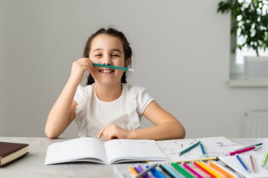 Sevimli küçük kız evde çalışıyor ve gülümsüyor.