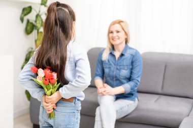 Çocuk kızı annemi tebrik ediyor ve ona çiçek laleleri veriyor. Anne ve kız gülümsüyor ve sarılıyorlar. Aile tatili ve birliktelik.