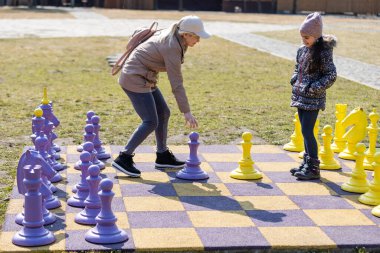 Küçük tatlı kız dışarıda dev satrançla oynuyor.