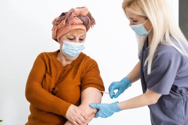 Hemşire yaşlı hastaya aşı yapıyor.