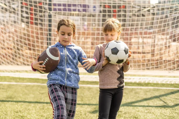 Kids play football on outdoor field. Children score a goal at soccer game. Girls kicking ball. Running child in team jersey and cleats. School football club. Sports training for young player.