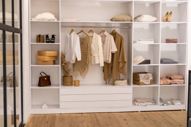 Giysiler beyaz gardıropta kutularla asılı.