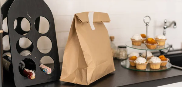 Pozadí obrázek řemeslné papírové tašky na dřevěném stole v bílém kuchyňském interiéru s etiketou Organic Food, donáška potravin, kopírovací prostor. — Stock fotografie