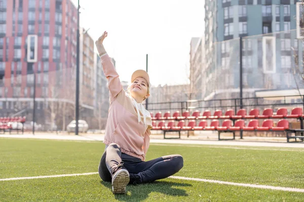 Młoda piękna blondynka fitness dziewczyna robi rozciąganie na stadionie. aktywność sportowa. Zielony stadion trawa na tle. — Zdjęcie stockowe