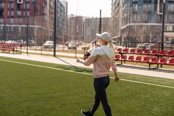 Młoda piękna blondynka fitness dziewczyna robi rozciąganie na stadionie. aktywność sportowa. Zielony stadion trawa na tle. — Zdjęcie stockowe