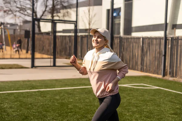 Szczęśliwa i uśmiechnięta kobieta fitness Jogging na stadionie. Ona ucieka. Sportowiec robi swoje rutynowe ćwiczenia sportowe na torze. — Zdjęcie stockowe