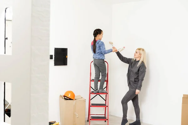 Mãe e filha felizes fazem reparos em casa. Sorrindo mulher e menina pintura na parede no quarto — Fotografia de Stock