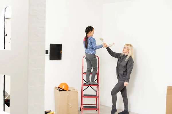 Happy mother and daughter makes repairs at home. Smiling woman and girl painting on wall at room Royalty Free Stock Images