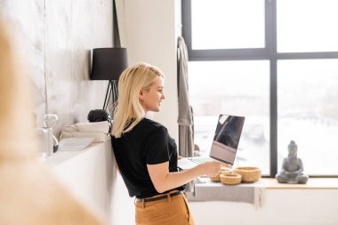 Genç ve güzel bir kadın evde dizüstü bilgisayar kullanıyor.