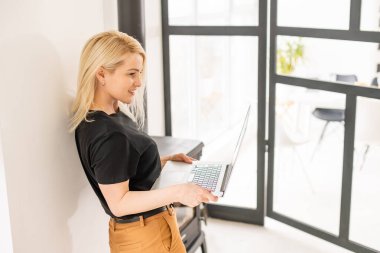 Genç ve güzel bir kadın evde dizüstü bilgisayar kullanıyor.