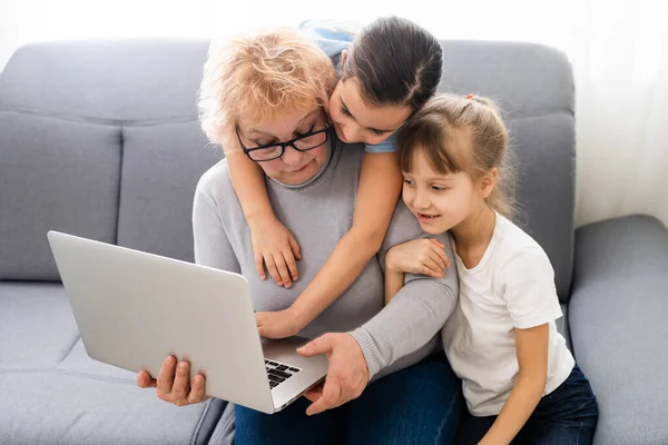 Grand-mère et deux petites-filles utilisent un ordinateur portable à la maison — Photo