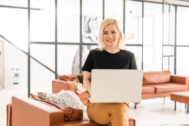 Uzaktan kumandalı ev işi, karantina sırasında serbest çalışma. Gülümseyen bayan rahat oturma odasında dizüstü bilgisayarda oturuyor ve çalışıyor.