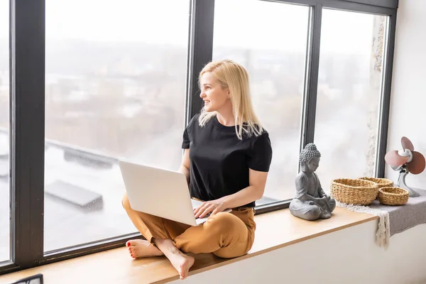 Gelukkig casual mooi vrouw werken op een laptop zitten in het huis. — Stockfoto