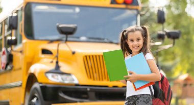 Otobüsün yanında duran sevimli kız okula gidiyor. Kameraya yakın çekim pozu veriyor.