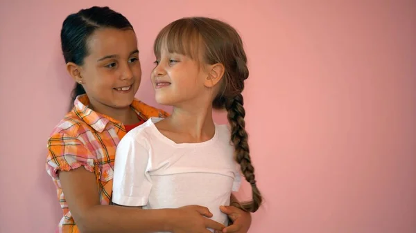 Dos chicas felices abrazándose aisladas sobre fondo rosa — Foto de Stock