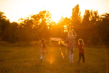 Anneler ve kızları gün batımında bir tarlada uçurtmayla