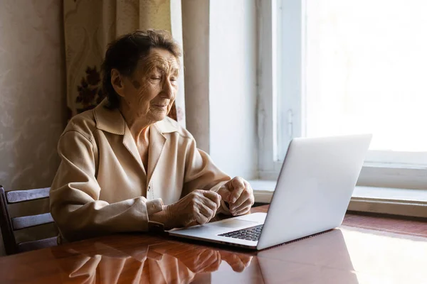 Старша жінка використовує ноутбук. Вона дуже здивована. Серфінг у браузері та соціальних мережах. Ноутбук на столі. Використання технології в концепції старості — стокове фото