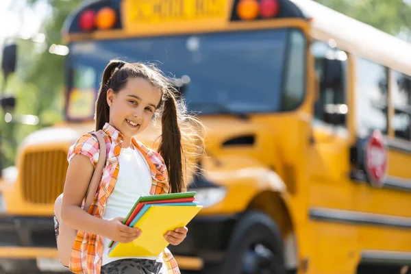 Schattig klein schoolmeisje in de buurt van schoolbus en kijken naar camera — Stockfoto