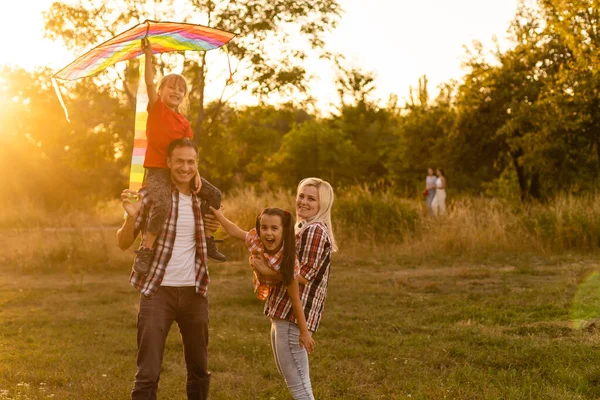 Feliz familia padre de madre e hijas lanzar una cometa en la naturaleza al atardecer — Foto de Stock