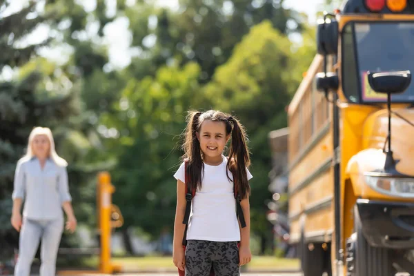 Mamá lleva a su hija a la escuela cerca del autobús escolar. de vuelta a la escuela — Foto de Stock