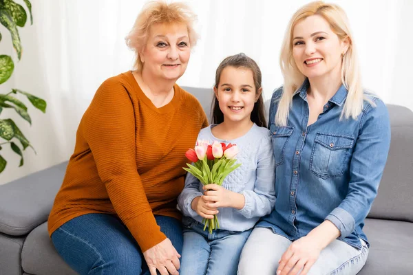Foto retrato de la nieta felicitando a la abuela dando tulipanes montón sentado cerca de mamá —  Fotos de Stock