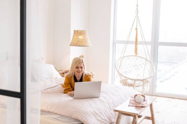 Genç ve güzel bir kadın evde dizüstü bilgisayar kullanıyor.