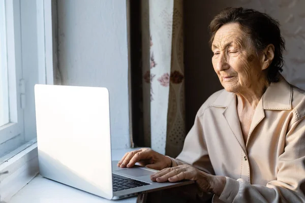 Mulher sênior usar laptop. Ela parece muito surpreendida. Navegar em um navegador e redes sociais. Laptop na mesa. Usando a tecnologia no conceito de velhice — Fotografia de Stock