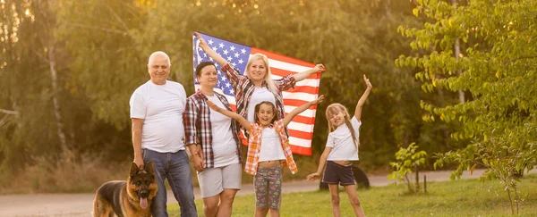 La gran familia está caminando banderas americanas. Vista frontal, patriotas americanos en el prado del parque. — Foto de Stock