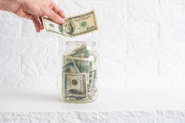 Cam kavanozdaki dolarlar. Erkeklerin kavanoza dolar koyduğu bir manzara. Evde para biriktirme kavramı.