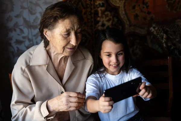 Granny and granddaughter. A cute little girl shows her grandmother a smartphone. — Stock Photo, Image