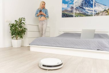 Robotik elektrik süpürgesini kontrol etmek için cep telefonu kullanan kadın