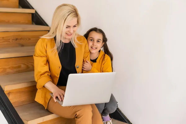Conceito de compras online ou pagamentos. Mãe ensina sua filha usando laptop em casa. Sentado nos degraus da escada — Fotografia de Stock
