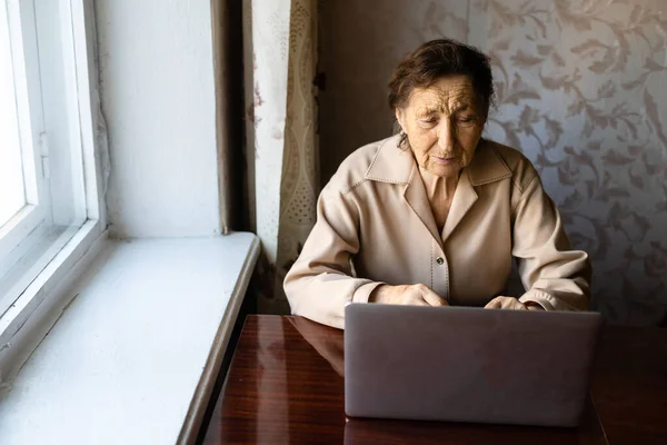 Старша жінка використовує ноутбук. Вона дуже здивована. Серфінг у браузері та соціальних мережах. Ноутбук на столі. Використання технології в концепції старості — стокове фото
