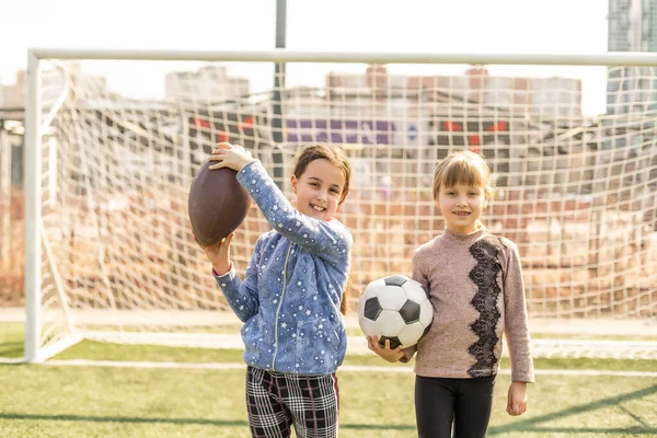 Kids play football on outdoor field. Children score a goal at soccer game. Girls kicking ball. Running child in team jersey and cleats. School football club. Sports training for young player.