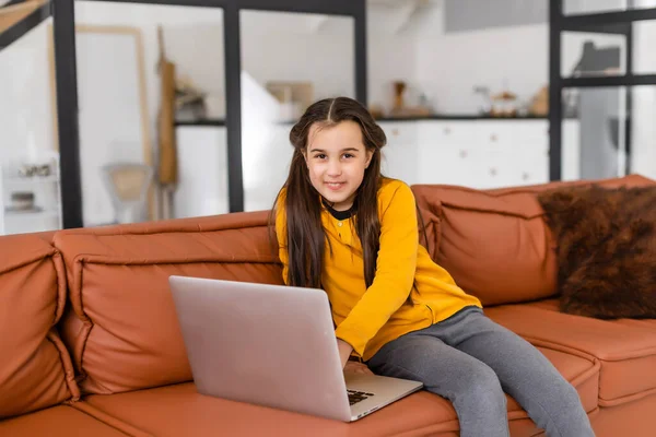 Menina inteligente faz lição de casa em sua sala de estar. Ela está sentada e usa laptop. — Fotografia de Stock