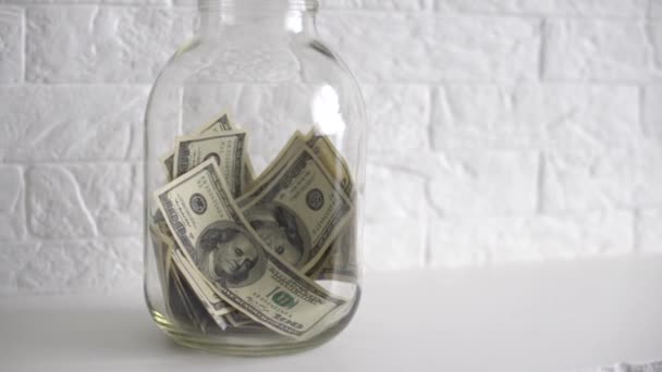 Hand putting a dollar bill in a savings jar with a white label — Stock Video