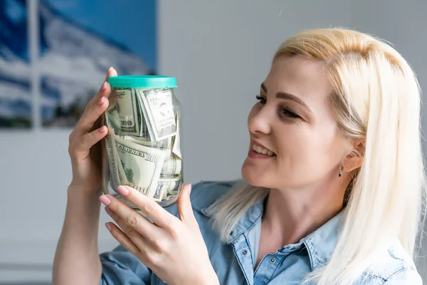 Mujer feliz en jersey gris banco de espera con dinero en efectivo en dólares, mirando a la cámara, aislado sobre fondo beige — Foto de Stock