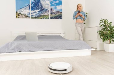Kadın dinlenirken robotik süpürge odayı temizliyor.