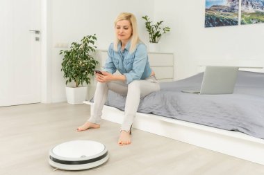 Kadın dinlenirken robotik süpürge odayı temizliyor.