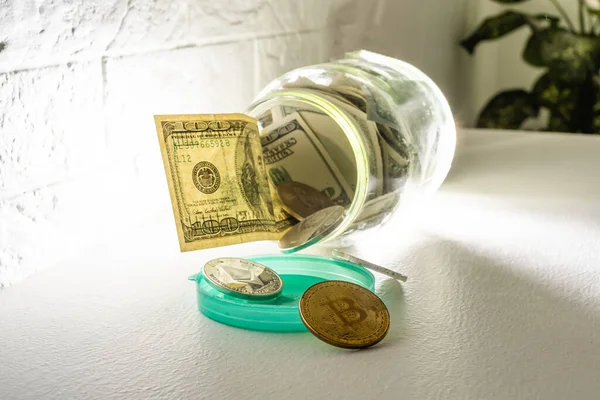 Bitcoin pièce d'or en bronze dans un bocal en verre sur fond blanc. Un ensemble de cryptomonnaies avec de vrais dollars dans un bocal en verre. Épargne, placements, concept de risque financier — Photo