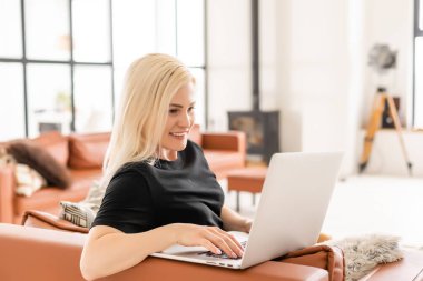 Genç ve güzel bir kadın evde dizüstü bilgisayar kullanıyor.