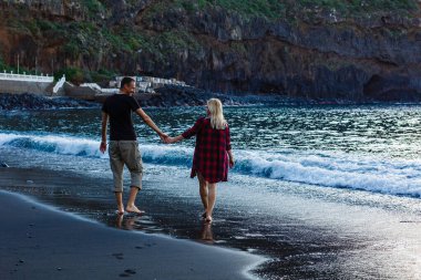 Kumsalda birlikte yürüyen tatilci çift birbirine sarılıyor. Mutlu ırklar arası genç çift, Asyalı kadın ve beyaz adam.