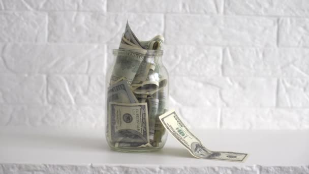 Dólares en un frasco de vidrio. Una vista de la mano del hombre poniendo dólares en el banco del frasco. Un concepto de ahorro de dinero en casa. — Vídeos de Stock