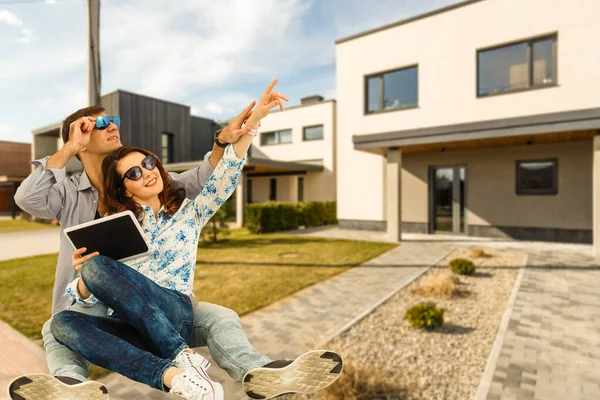 Glückliches Paar mit dem neuen Haus im Hintergrund und lächelnd — Stockfoto