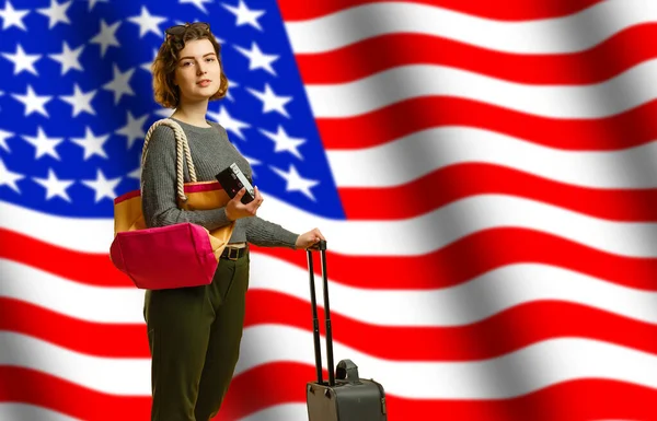 Девушка-студентка улыбается, держа рюкзак и флаг США изолированы на сером фоне, копировальное пространство, концепция студенческого обмена. Портрет милой студентки на тёмном фоне с флагом Америки — стоковое фото