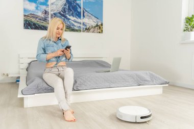 Robotik elektrik süpürgesini kontrol etmek için cep telefonu kullanan kadın