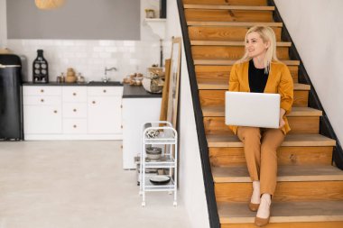 Uzaktan kumandalı ev işi, karantina sırasında serbest çalışma. Gülümseyen bayan rahat oturma odasında dizüstü bilgisayarda oturuyor ve çalışıyor.