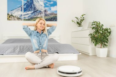 Kadın dinlenirken robotik süpürge odayı temizliyor.