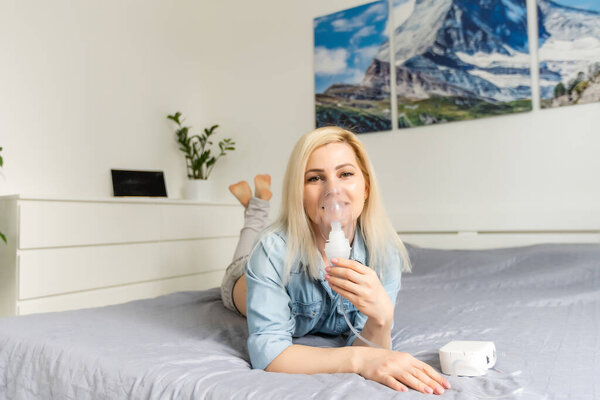 Больная красивая женщина в синей ткани держит маску носа с респираторными проблемами в больничной палате. женщина ингаляционная терапия с помощью маски ингалятора с мягким потоком дыма от бронходилататора.