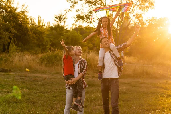 Счастливая семья отец матери и дочери запускают воздушного змея на природе на закате — стоковое фото